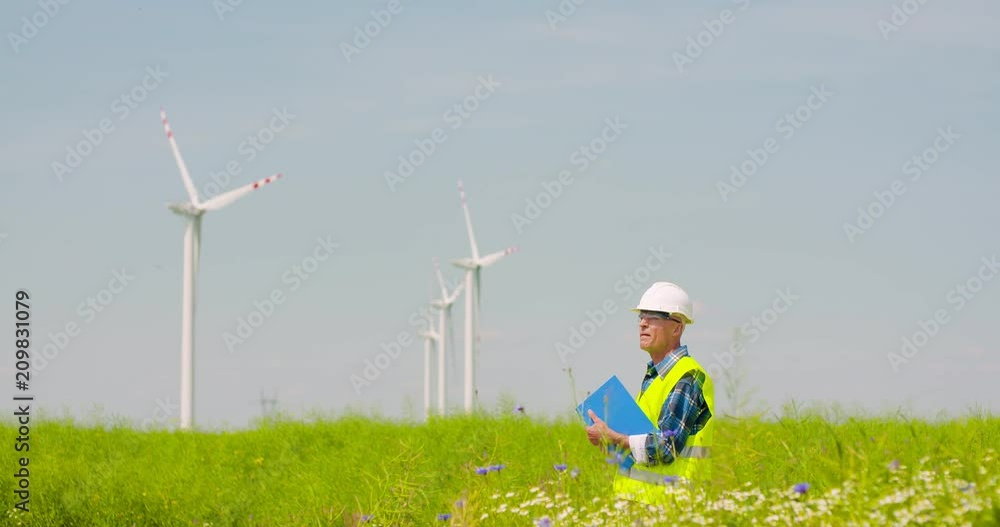 Engineer Writing On Clipboard While Standing Against Windmill Engineer Writing On Clipboard While Standing Against Windmill