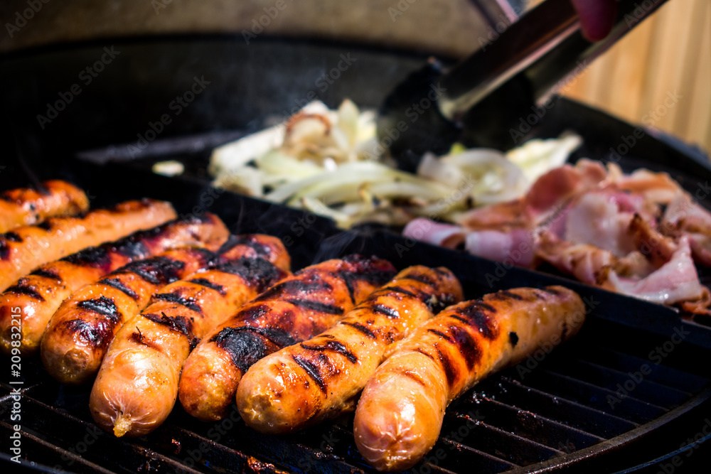 A bbq with sausages, bacon and onion cooking in summer