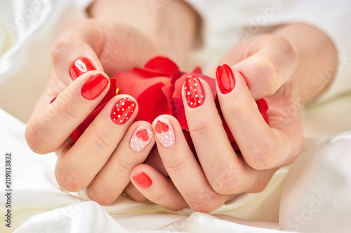 Female manicured hands with rose petals. Young woman hands holding pile of red rose petals. Lady in beauty salon.