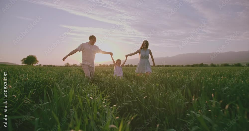 Happy caucasian family of three going through summer or spring field in the sunset 4k Happy caucasian family of three going through summer or spring field in the sunset 4k