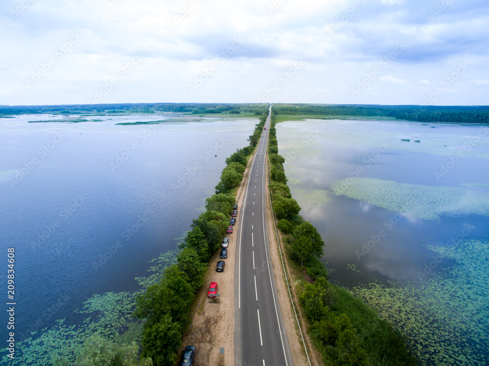 Landscape of an asphalt road. View from above on the road going along the blue river. Summer photography with bird's eye view