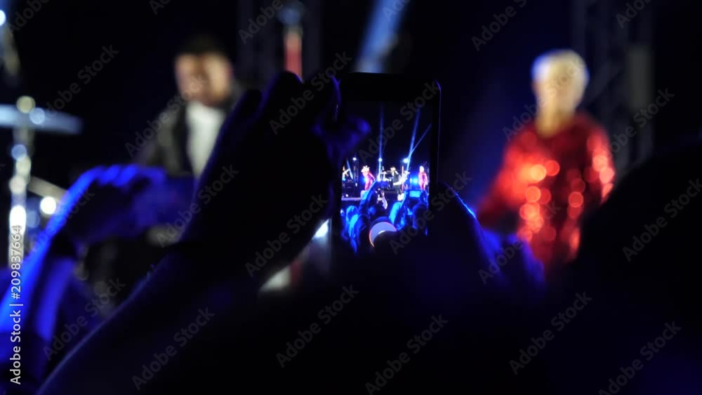 Fan spectator stay by concert stage hold mobile phone shooting video of music performance in night lights lumiere