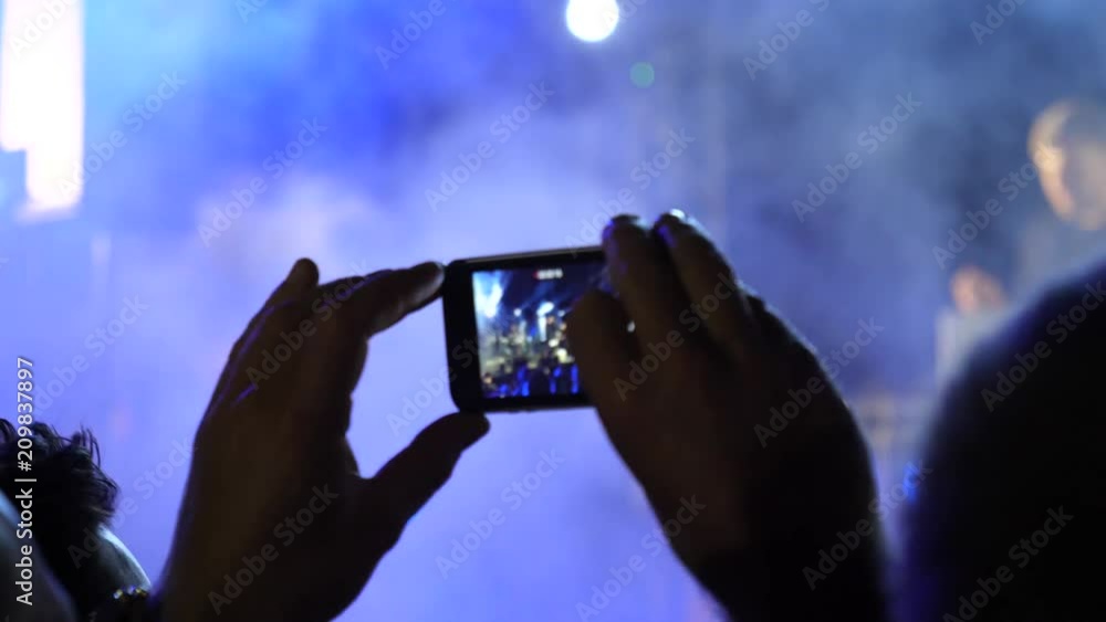 Fan spectator stay by concert stage hold mobile phone shooting video of music performance in night lights lumiere