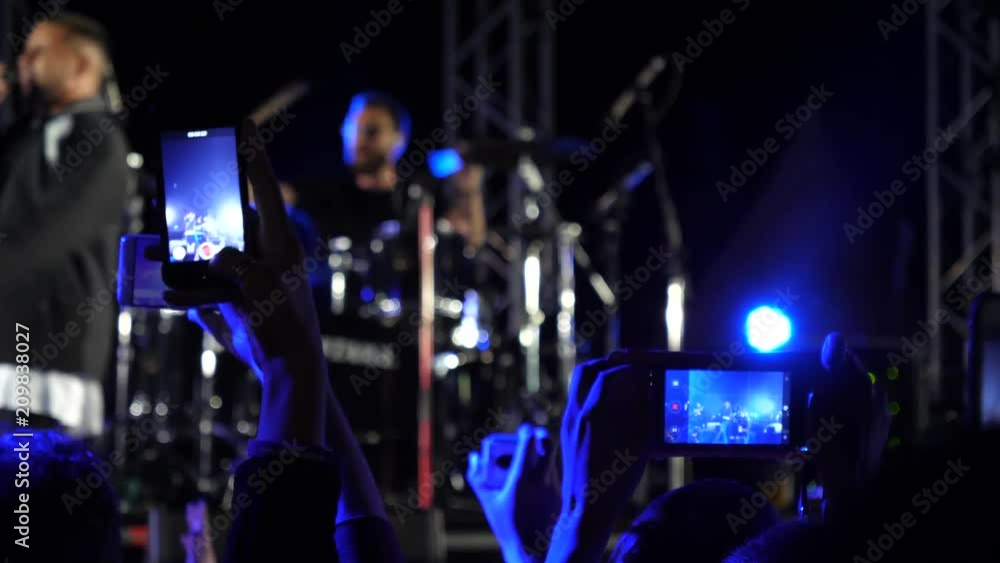 Fan spectators stay by concert stage hold mobile phones shooting video of music performance in night lights lumiere
