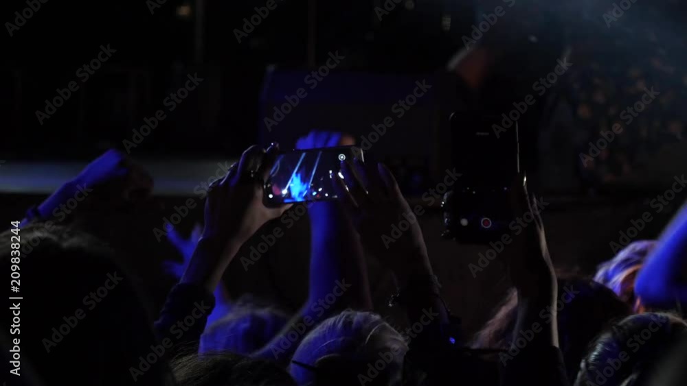 Fan spectators stay by concert stage hold phones shooting video of music performance in night lights lumiere