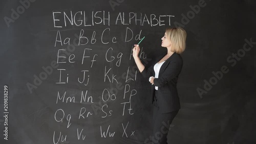 Teacher is writing letter of alphabet on blackboard with chalk. Education in elementary school concept. photo