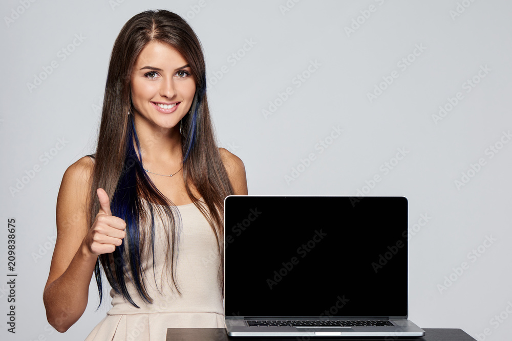 Happy woman showing blank black laptop computer screen, looking at camera and giving thumb up Happy woman showing blank black laptop computer screen, looking at camera and giving thumb up