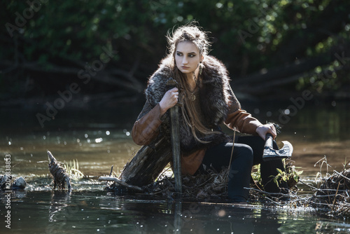 Fototapeta Viking woman with sword and hammer wearing traditional warrior clothes in a deep mysterious forest