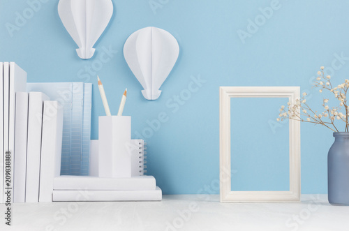 Modern style home workplace - white stationery  blank  frame  flowers on soft blue background and light desk.