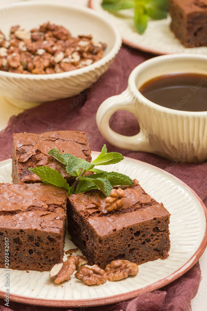 Brownie sweet chocolate dessert with walnuts and meant leaves on craft plate and cup of black coffee. Brownie sweet chocolate dessert with walnuts and meant leaves on craft plate and cup of black coffee.