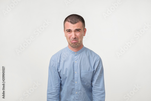 Studio shot of young handsome man, pouting and crying, complaining about girlfriend.