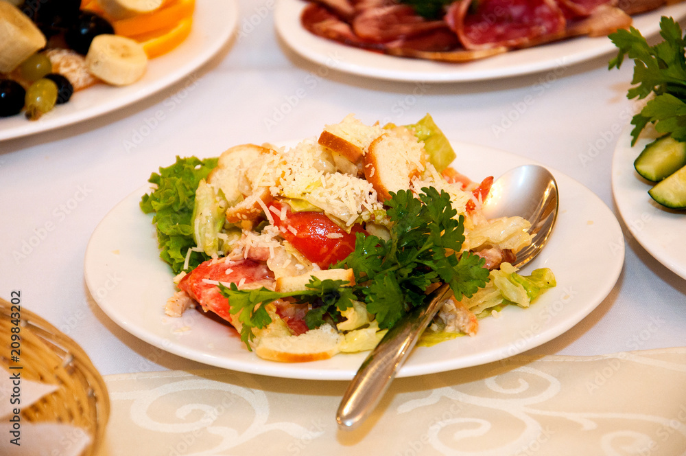 Salad with tomatoes, chicken, croutons and greens in a white plate with a spoon, on a табл. Salad with tomatoes, chicken, croutons and greens in a white plate with a spoon, on a табл.
