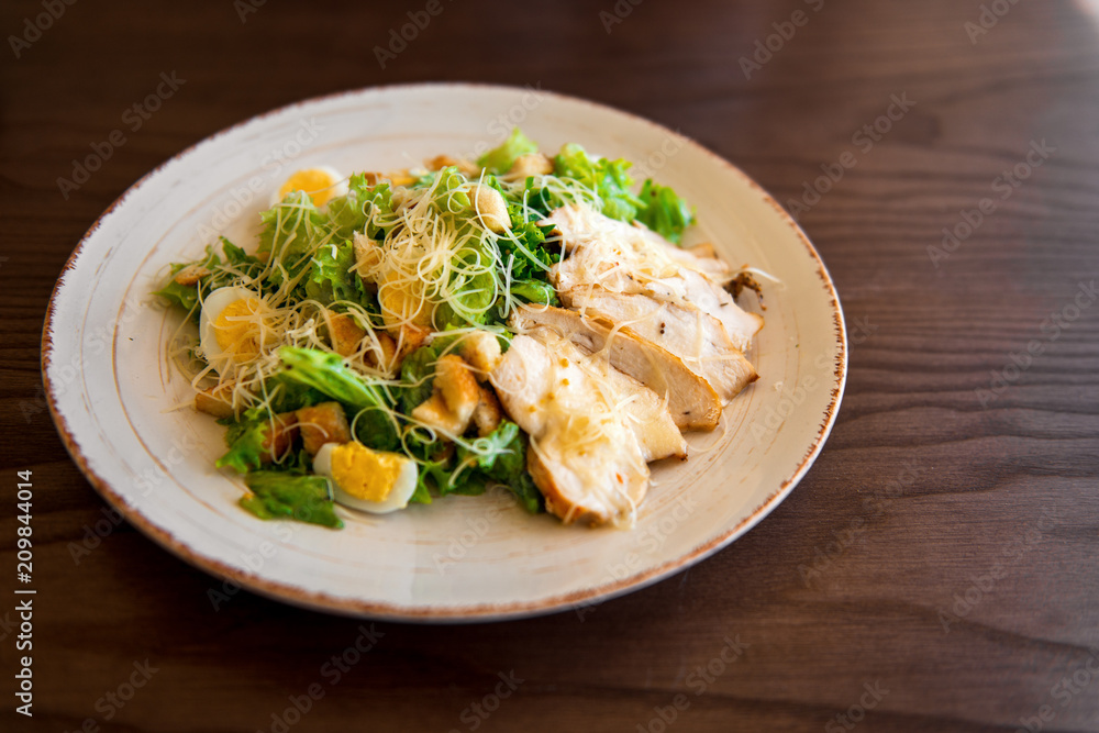 Fresh summer salad Ceasar with eggs, lettuce, chicken and parmesan cheese on white plate on wooden background; healthy concept; side view Fresh summer salad Ceasar with eggs, lettuce, chicken and parmesan cheese on white plate on wooden background; healthy concept; side view