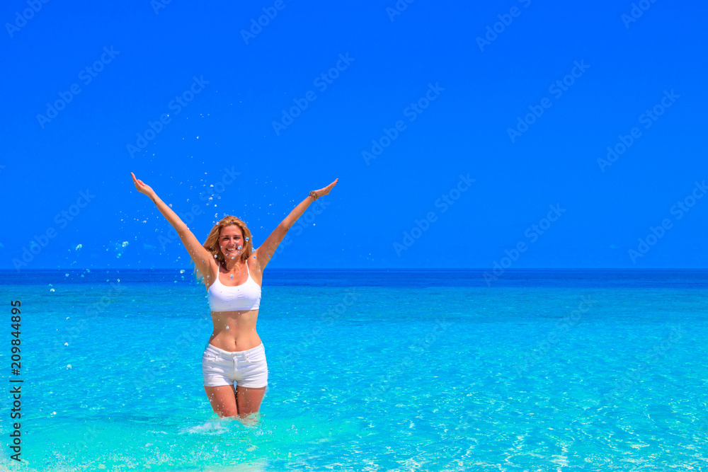 Gorgeous blond woman with white clothes is standing in the water at the sandy beach Gorgeous blond woman with white clothes is standing in the water at the sandy beach