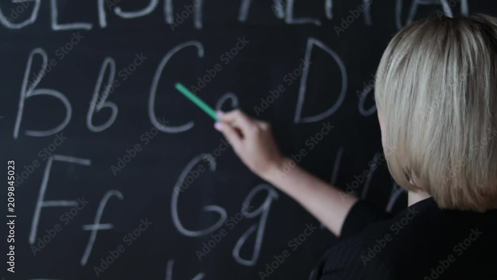Teacher is writing letter of alphabet on blackboard with chalk. Education in elementary school concept. Teacher is writing letter of alphabet on blackboard with chalk. Education in elementary school concept.