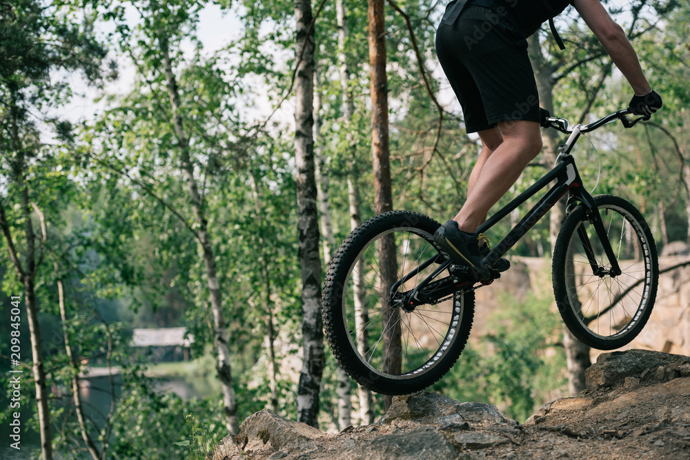Naklejka premium cropped image of male extreme cyclist jumping on mountain bike in forest