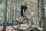 young male extreme cyclist in protective helmet riding on mountain bicycle in forest