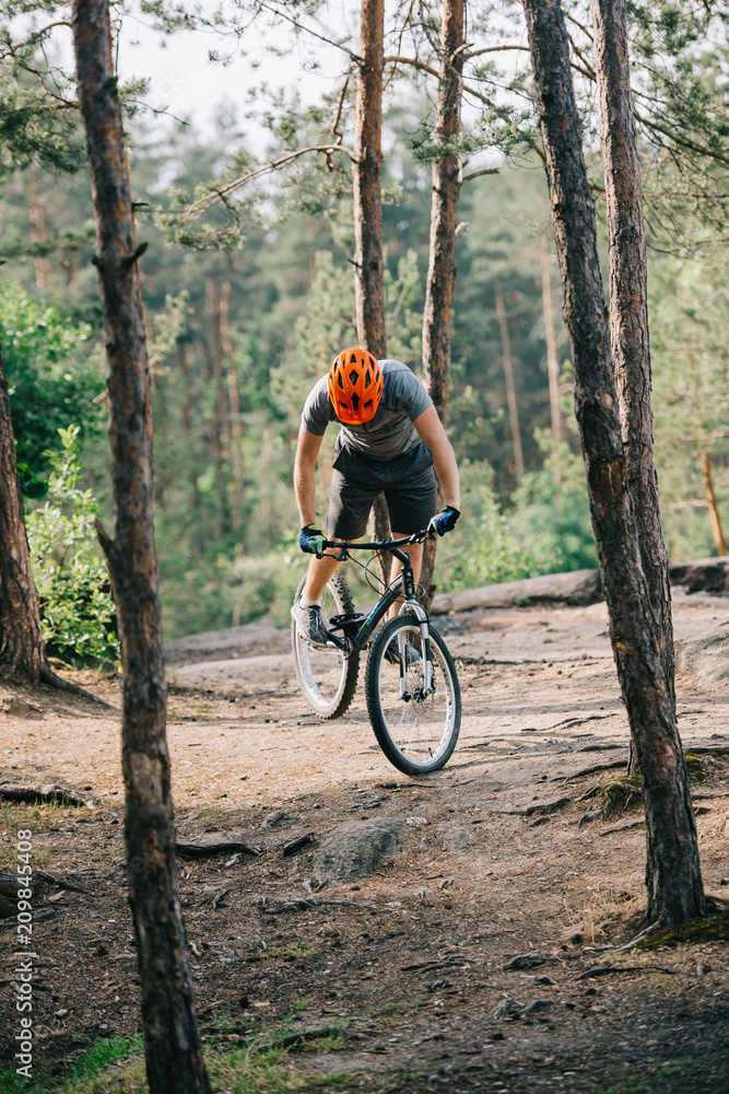 front view of male extreme cyclist in protective helmet doing stunt on mountain bicycle in forest