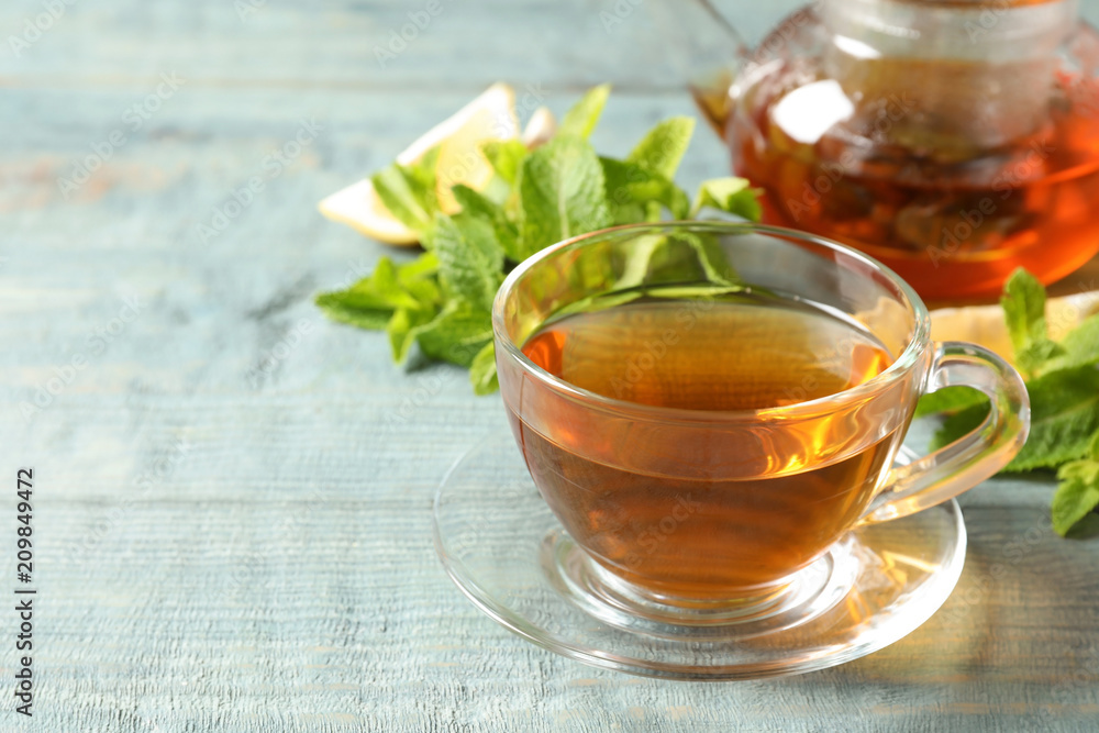 Cup with hot aromatic mint tea and fresh leaves on table Cup with hot aromatic mint tea and fresh leaves on table