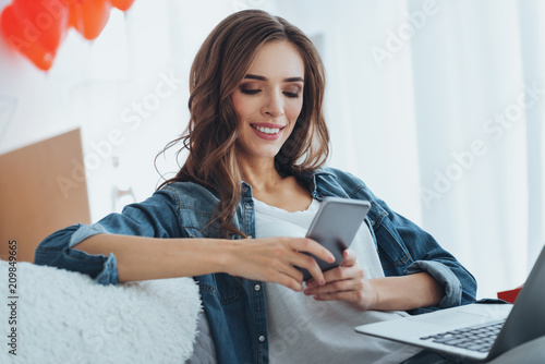 Social networks. Smart happy woman holding her smartphone while checking messages from social networks
