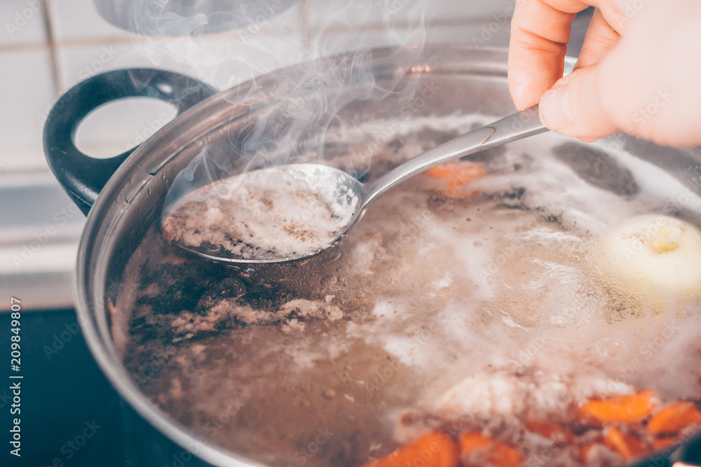Cook with a spoon removes the foam from the boiling soup in a saucepan Cook with a spoon removes the foam from the boiling soup in a saucepan