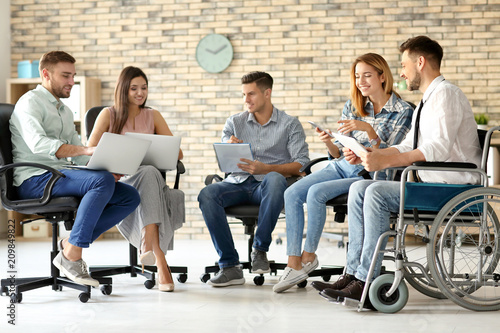 Young man in wheelchair with colleagues at workplace