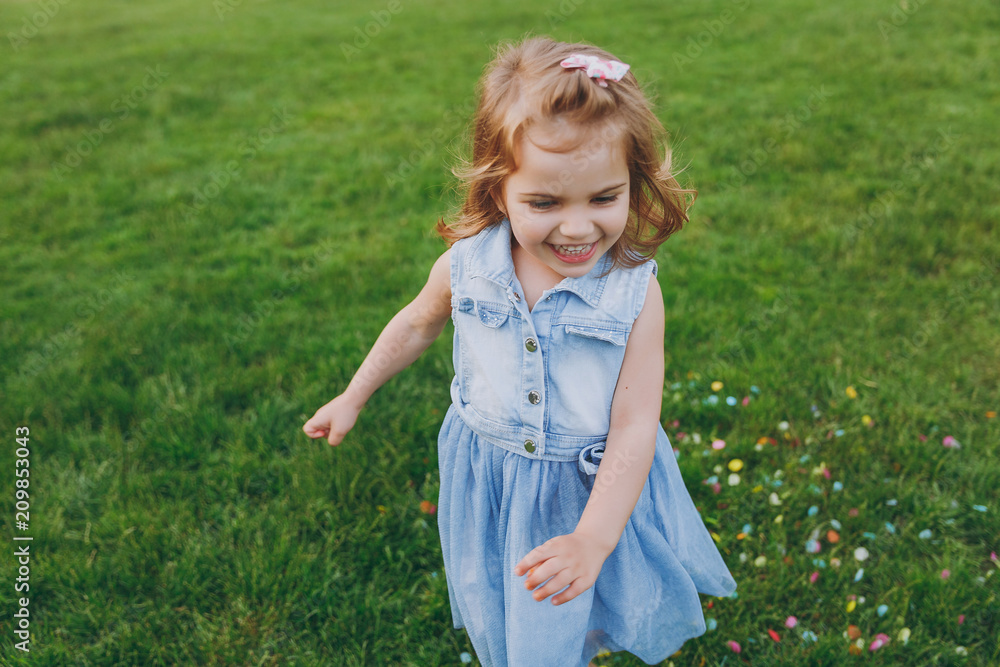 Smiling little cute child baby girl in denim dress walking and running, have fun on green grass lawn in park. Mother, little kid daughter. Mother's Day, love family, parenthood, childhood concept. Smiling little cute child baby girl in denim dress walking and running, have fun on green grass lawn in park. Mother, little kid daughter. Mother's Day, love family, parenthood, childhood concept.
