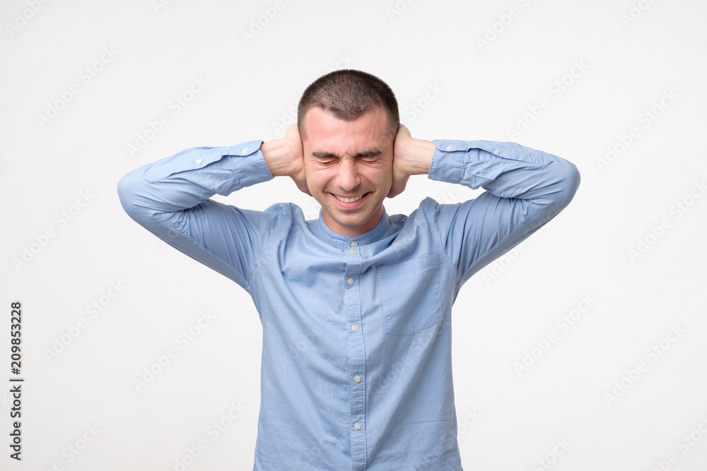Stressed frustrated young man plugging his ears and keeping eyes closed. Stressed frustrated young man plugging his ears and keeping eyes closed.
