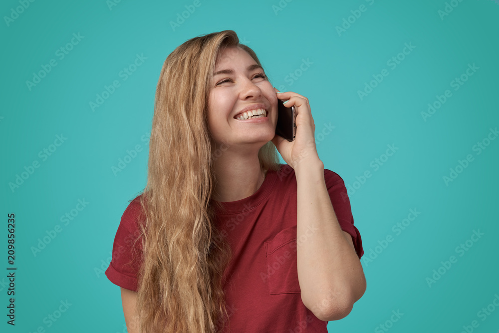 Portrait of a happy smiling woman in red t-shirt holding mobile phone isolated on the blue background. Happy Modern Girl Talking on the Phone and Laughing. Copy Space Portrait of a happy smiling woman in red t-shirt holding mobile phone isolated on the blue background. Happy Modern Girl Talking on the Phone and Laughing. Copy Space