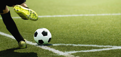 Foot of a child football player and ball on the football field, kicking a corner kick