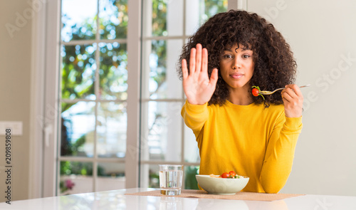 African american woman eating pasta salad with open hand doing stop sign with serious and confident expression  defense gesture