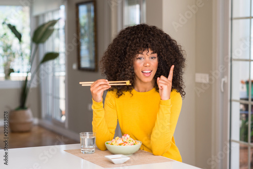 African american woman eating asian rice at home surprised with an idea or question pointing finger with happy face, number one
