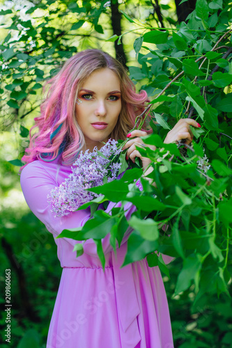 Beautiful girl with colorful dyed hair and perfect makeup and hairstyle standig next to lilac bush © Smile