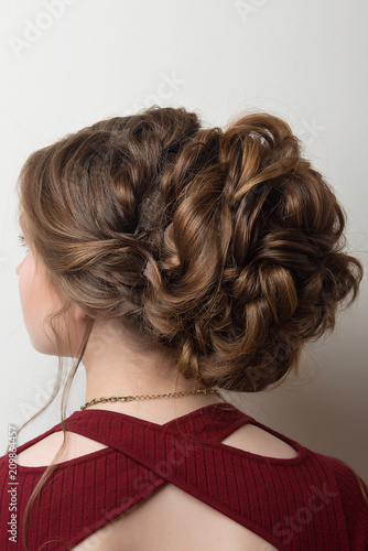 Wedding hairstyle bun on the head of brown-haired women on a gray background close-up rear vie