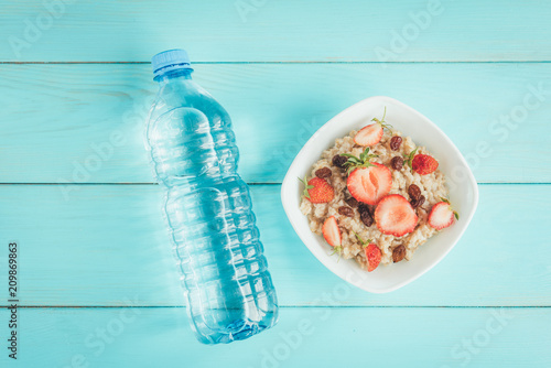 Bottle of water, oatmeal with strawberry and raisins on blue background. Healthy lifestyle, fitness, food
