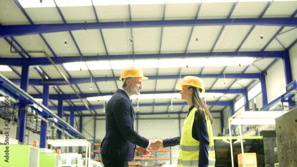 Industrial man and woman engineers in a factory, shaking hands. Industrial man and woman engineers in a factory, shaking hands.