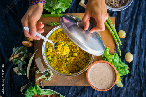 Woman hands tastes pot with cooked bulgur wheat grain porridge with turmeric powder, garlic and spices served for lunch or dinner. Traditional arabic, asian, middle east. Vegan vegetarian healthy food