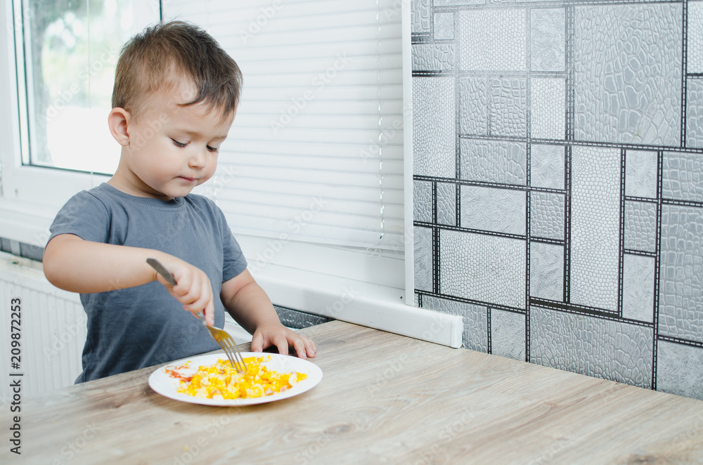 a child in a t-shirt in the kitchen eating an omelet, a fork