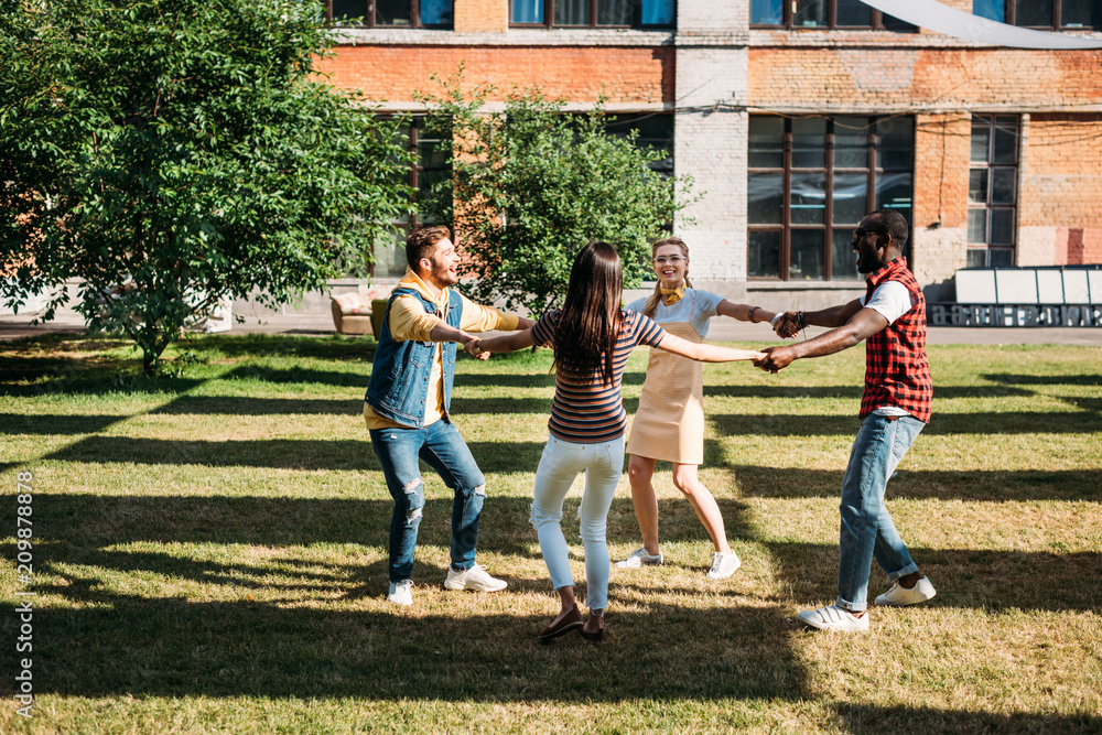 Fototapeta premium multicultural young friends holding hands while having fun together on summer day