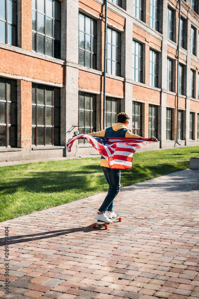 back view of man with american flag skating on longboard on street