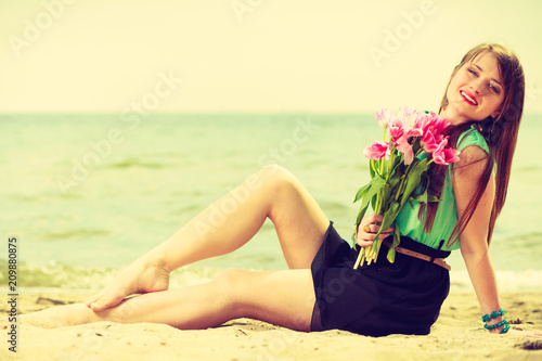 Woman holding bouquet of flowers sitting on beach