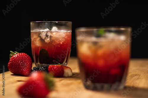 Bonito cóctel con zarzamoras, fresas y hojas de menta en un bonito vaso de vidrio sobre un fondo negro y de madera