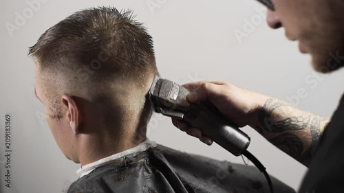 Tattoed barber makes haircut for customer at the barber shop by using hairclipper, man's haircut and shaving at the hairdresser, barber shop photo