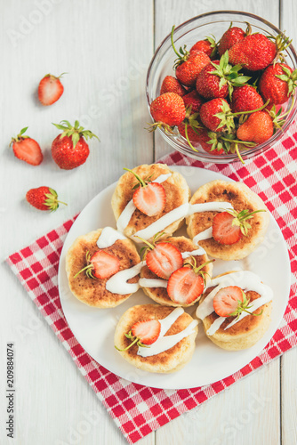 Homemade cottage cheese pancakes with sour cream and fresh strawberry on white wooden background. Healthy breakfast.