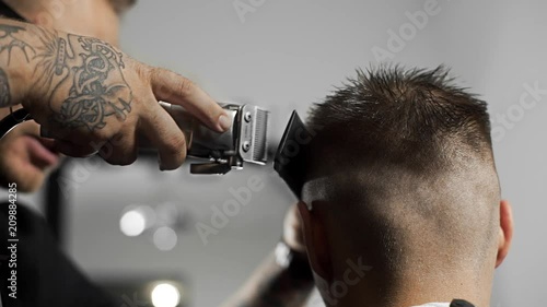Tattoed barber makes haircut for customer at the barber shop by using hairclipper, man's haircut and shaving at the hairdresser, barber shop photo