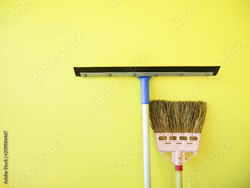 Floor squeegee rubber blade and sweeping broom beside the yellow wall. photo