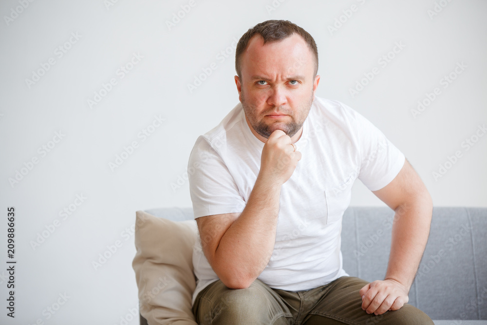 Image of man in white T-shirt sitting on sofa Image of man in white T-shirt sitting on sofa