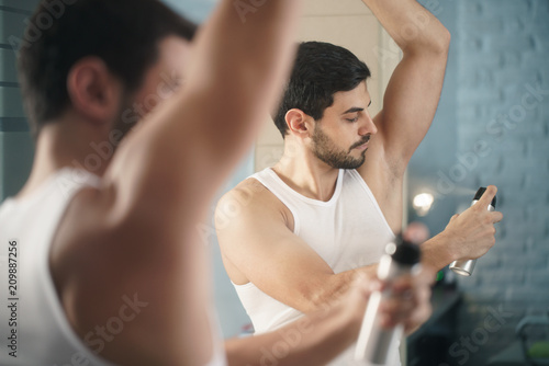 Man Using Spray Deodorant On Underarm For Bad Smell