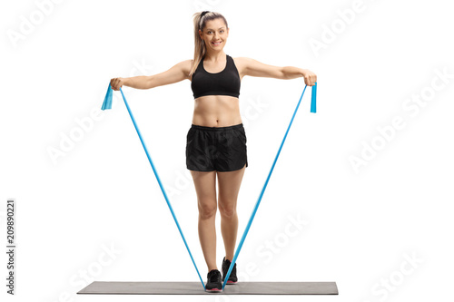 Young woman standing on an exercise mat and exercising with a rubber band