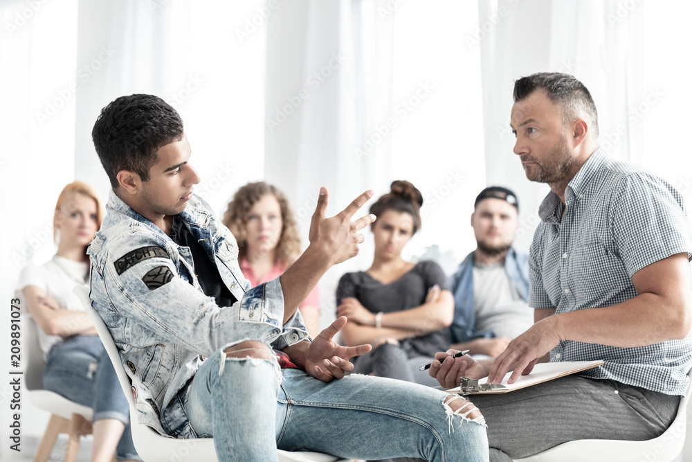 Mixed-race teenager talking to a school counselor in detention. Blurred classmates in the background Mixed-race teenager talking to a school counselor in detention. Blurred classmates in the background